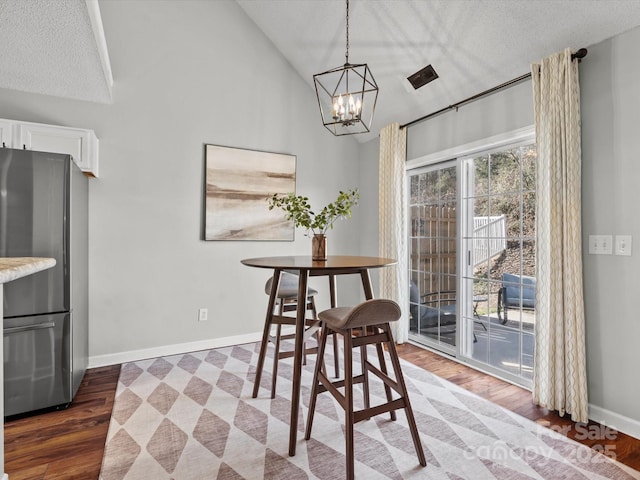 dining room featuring a textured ceiling, dark hardwood / wood-style flooring, an inviting chandelier, and vaulted ceiling