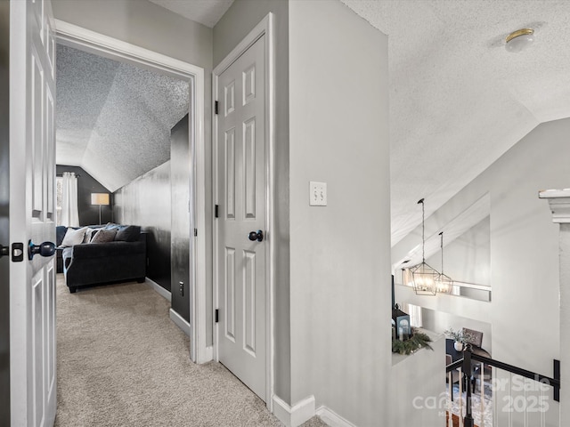 corridor featuring a textured ceiling, a chandelier, vaulted ceiling, and light colored carpet