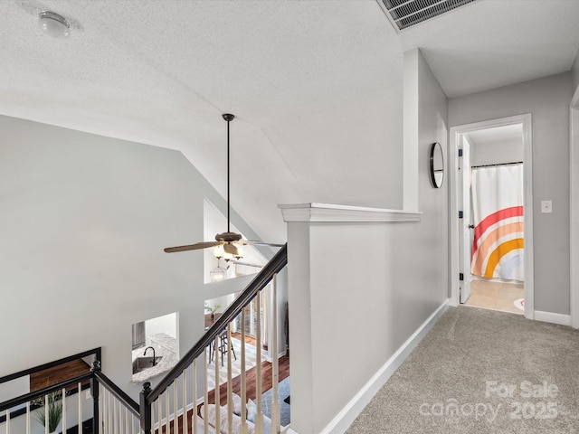 hall featuring lofted ceiling, light colored carpet, and a textured ceiling