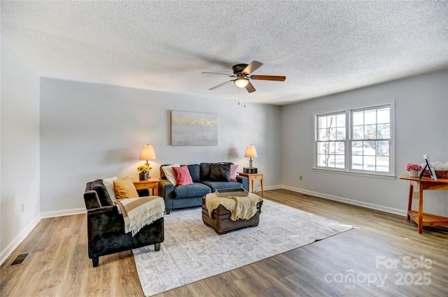 living room with ceiling fan, a textured ceiling, and light wood-type flooring