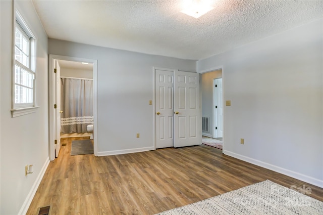 unfurnished bedroom with ensuite bathroom, wood-type flooring, and a textured ceiling