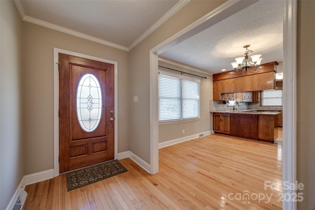 foyer with light wood-type flooring, ornamental molding, a textured ceiling, and a notable chandelier