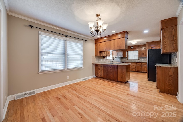 kitchen with pendant lighting, black refrigerator, light hardwood / wood-style flooring, tasteful backsplash, and kitchen peninsula