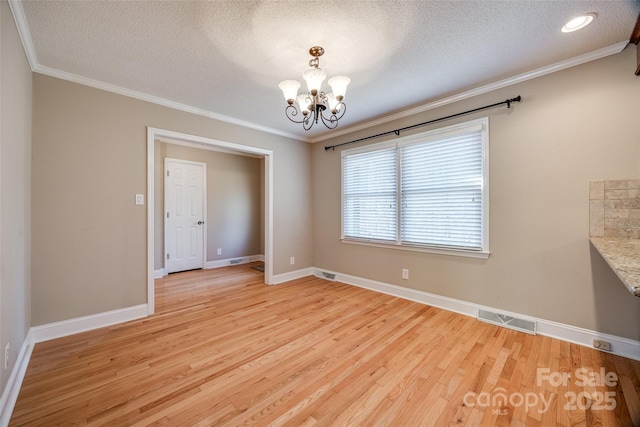 unfurnished dining area with crown molding, light wood-type flooring, a textured ceiling, and a chandelier