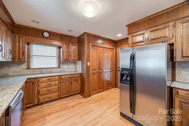 kitchen with backsplash, light stone counters, light hardwood / wood-style flooring, and appliances with stainless steel finishes