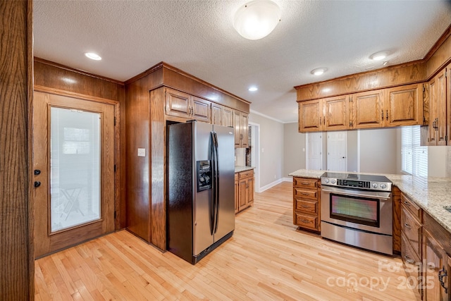 kitchen featuring light stone countertops, appliances with stainless steel finishes, kitchen peninsula, crown molding, and light hardwood / wood-style flooring