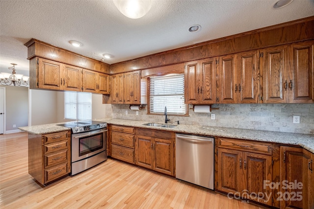 kitchen with sink, light wood-type flooring, appliances with stainless steel finishes, kitchen peninsula, and a chandelier