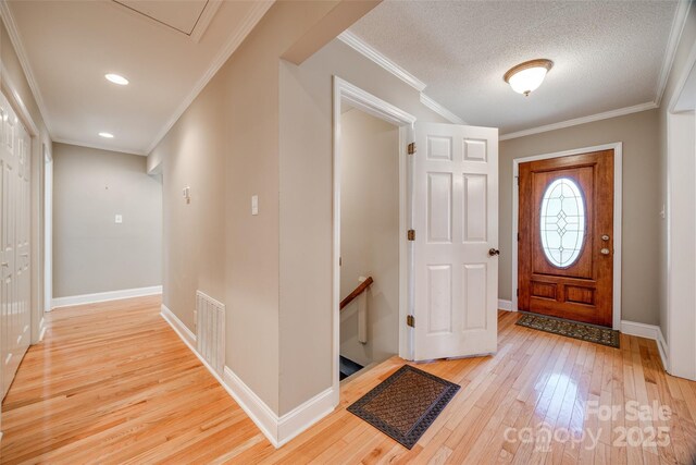 foyer entrance with a textured ceiling, light wood-type flooring, and ornamental molding