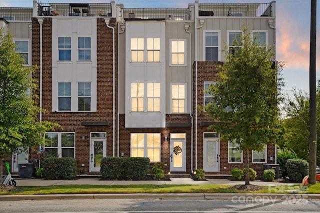 townhome / multi-family property featuring central AC unit, board and batten siding, and brick siding