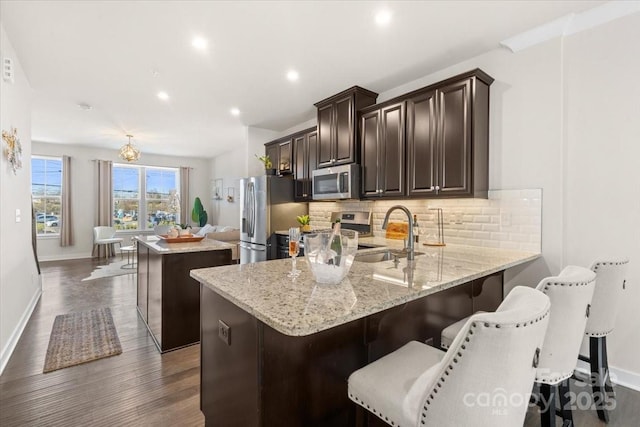 kitchen with a center island, stainless steel appliances, decorative backsplash, a sink, and dark brown cabinets