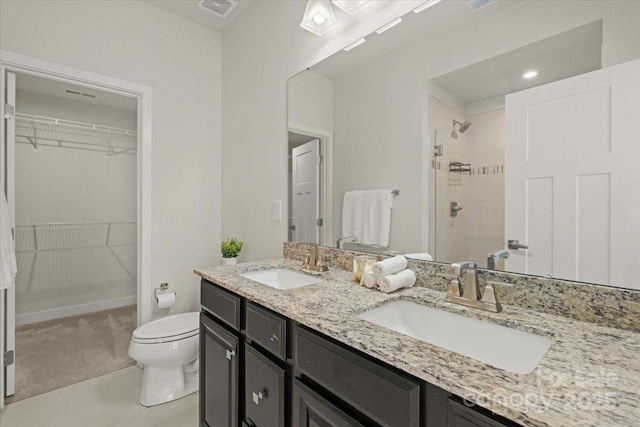 full bath featuring a walk in closet, tiled shower, a sink, and toilet