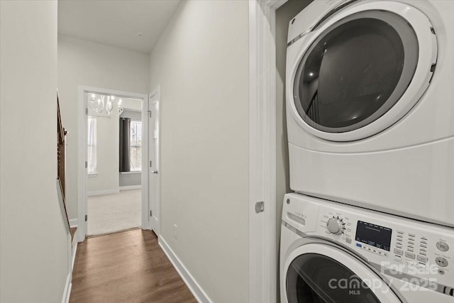 laundry room with laundry area, wood finished floors, stacked washer and clothes dryer, and baseboards