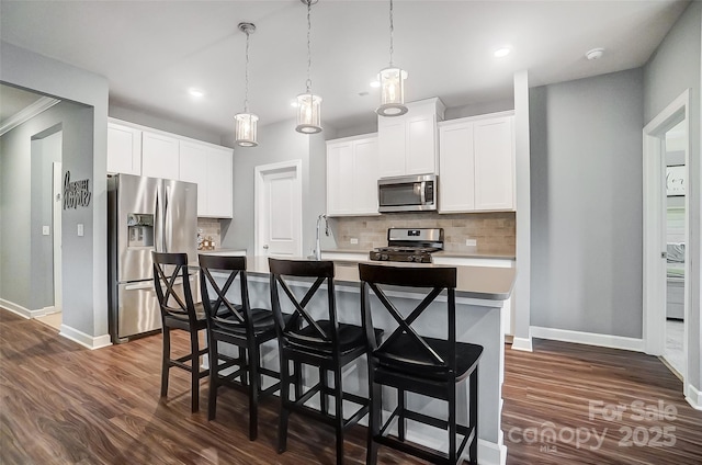 kitchen with stainless steel appliances, a kitchen breakfast bar, decorative light fixtures, a kitchen island with sink, and white cabinets