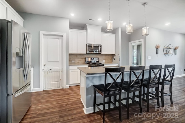 kitchen featuring hanging light fixtures, white cabinetry, a kitchen island with sink, and appliances with stainless steel finishes