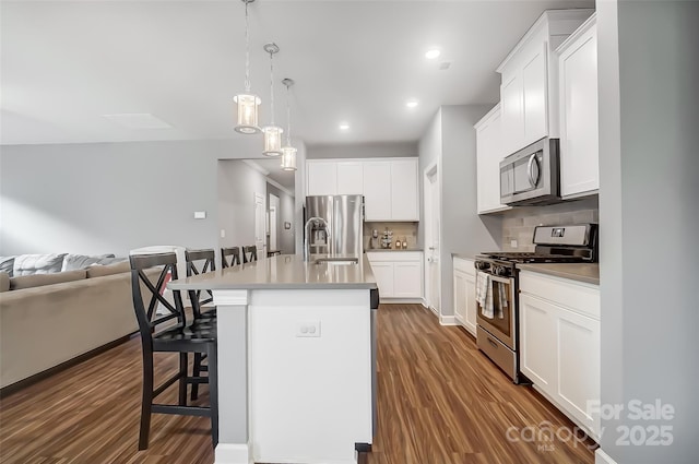 kitchen featuring stainless steel appliances, backsplash, a kitchen bar, a kitchen island with sink, and white cabinets