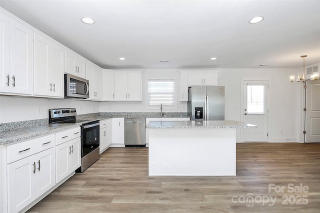 kitchen featuring decorative light fixtures, appliances with stainless steel finishes, white cabinetry, and a center island