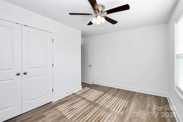 unfurnished bedroom featuring ceiling fan, a closet, hardwood / wood-style flooring, and multiple windows