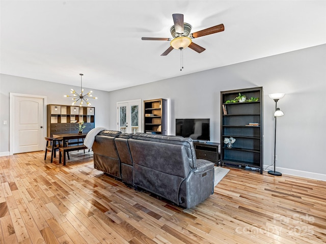 living room with ceiling fan with notable chandelier, french doors, and light hardwood / wood-style flooring