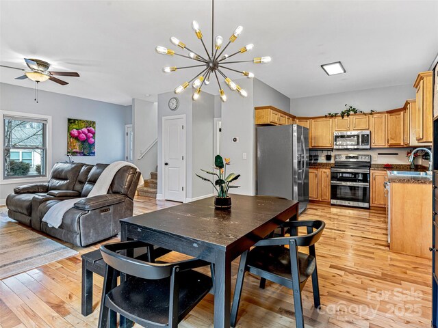 dining room with ceiling fan with notable chandelier, sink, and light hardwood / wood-style flooring