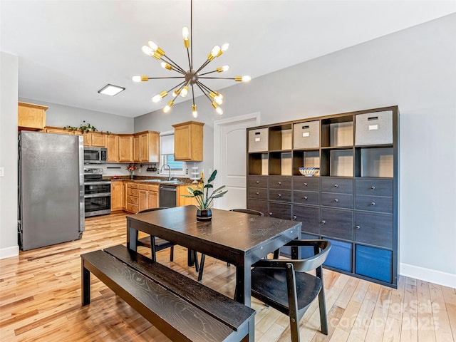 kitchen with appliances with stainless steel finishes, light brown cabinetry, sink, a notable chandelier, and light hardwood / wood-style floors