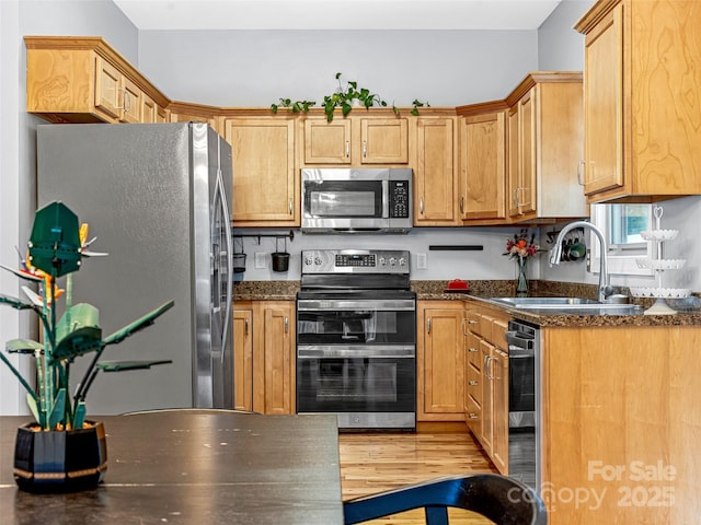 kitchen featuring dark stone counters, sink, light wood-type flooring, appliances with stainless steel finishes, and beverage cooler