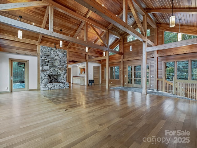 unfurnished living room with beamed ceiling, light hardwood / wood-style floors, a stone fireplace, and high vaulted ceiling