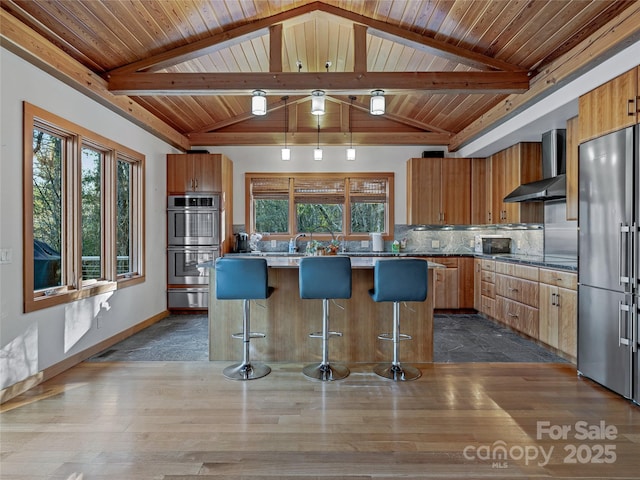 kitchen with tasteful backsplash, a kitchen island, a breakfast bar, stainless steel appliances, and wall chimney exhaust hood