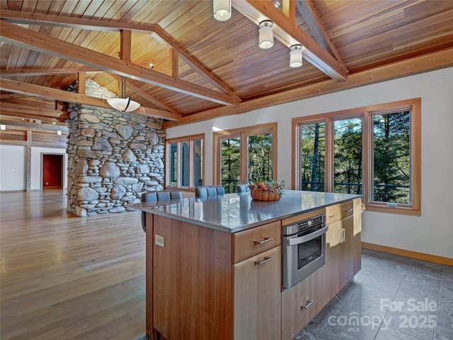 kitchen with stainless steel oven, vaulted ceiling with beams, wooden ceiling, and a kitchen island