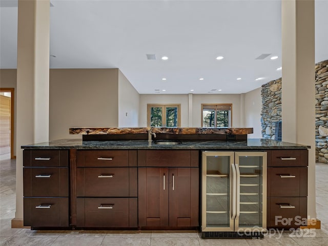 kitchen with sink, beverage cooler, dark brown cabinets, and dark stone counters