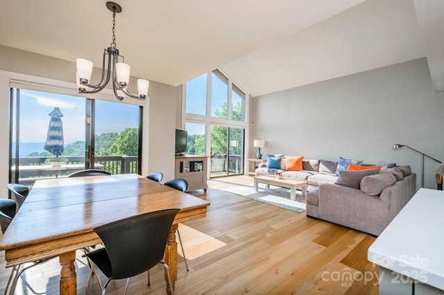 dining area with an inviting chandelier, high vaulted ceiling, and light hardwood / wood-style flooring