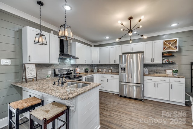 kitchen featuring appliances with stainless steel finishes, white cabinets, wall chimney range hood, and kitchen peninsula