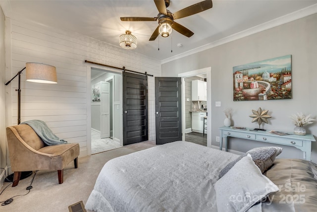 bedroom featuring a barn door, light carpet, ceiling fan, ornamental molding, and ensuite bathroom