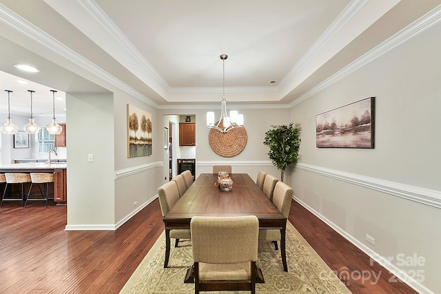 dining space featuring sink, a raised ceiling, dark hardwood / wood-style flooring, a notable chandelier, and ornamental molding