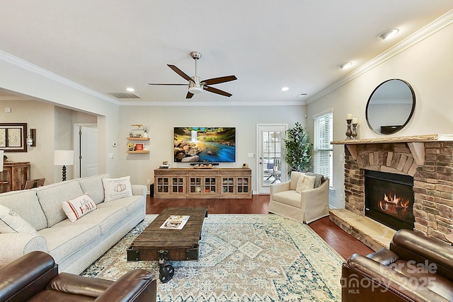 living room with hardwood / wood-style flooring, ceiling fan, a stone fireplace, and ornamental molding