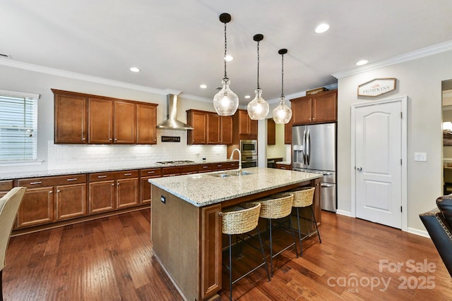 kitchen with sink, wall chimney exhaust hood, an island with sink, a kitchen bar, and appliances with stainless steel finishes