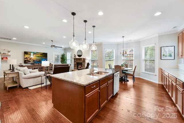 kitchen with sink, light stone counters, decorative light fixtures, a kitchen island with sink, and a fireplace