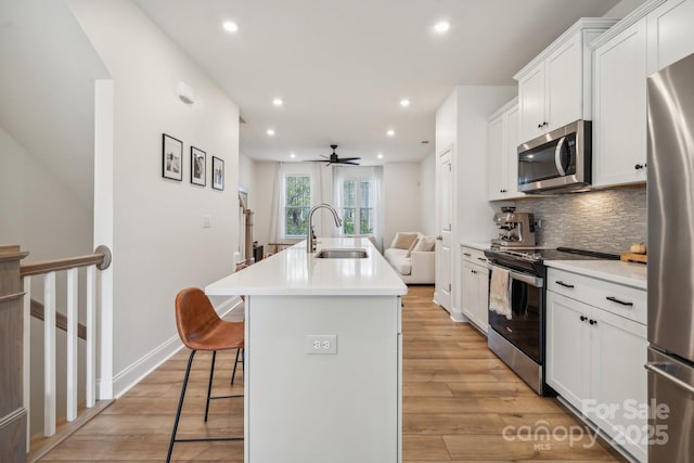 kitchen featuring sink, stainless steel appliances, white cabinetry, and an island with sink