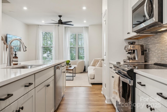 kitchen featuring light hardwood / wood-style floors, appliances with stainless steel finishes, white cabinetry, sink, and ceiling fan