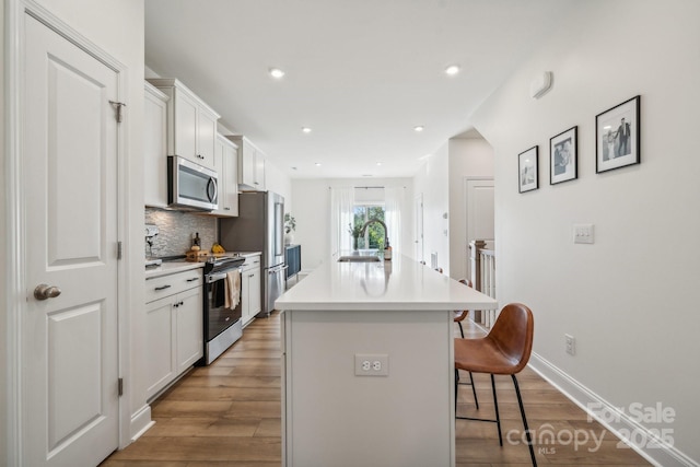 kitchen featuring a kitchen bar, appliances with stainless steel finishes, white cabinets, sink, and a center island with sink