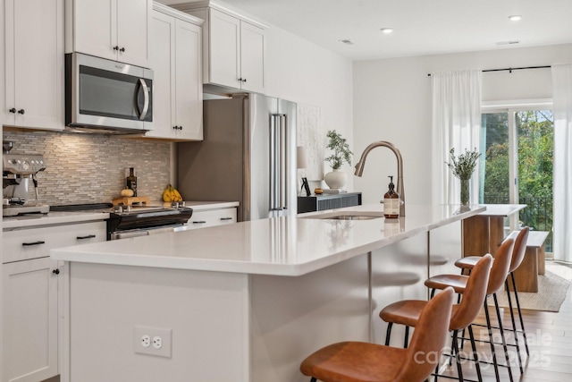 kitchen featuring stainless steel appliances, white cabinetry, a kitchen island with sink, and a breakfast bar