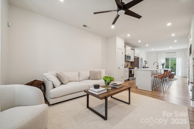 living room with ceiling fan, sink, and light wood-type flooring