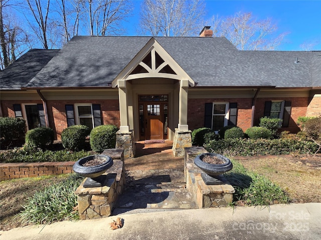 view of front facade featuring roof with shingles, a chimney, a fire pit, and brick siding