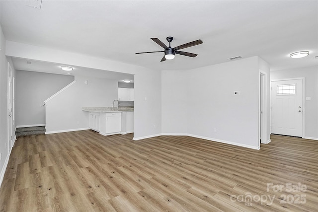 unfurnished living room featuring ceiling fan, sink, and light wood-type flooring