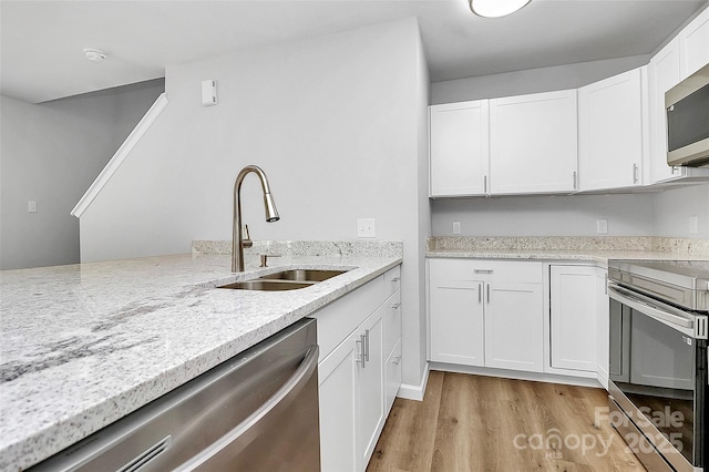 kitchen featuring light stone counters, stainless steel appliances, sink, light hardwood / wood-style flooring, and white cabinetry