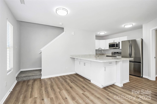 kitchen with light stone countertops, white cabinetry, sink, stainless steel appliances, and kitchen peninsula