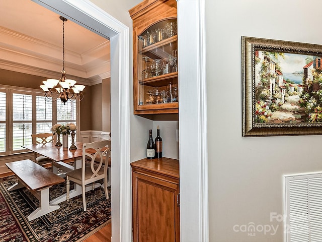 dining space with a tray ceiling, crown molding, wood-type flooring, and a notable chandelier