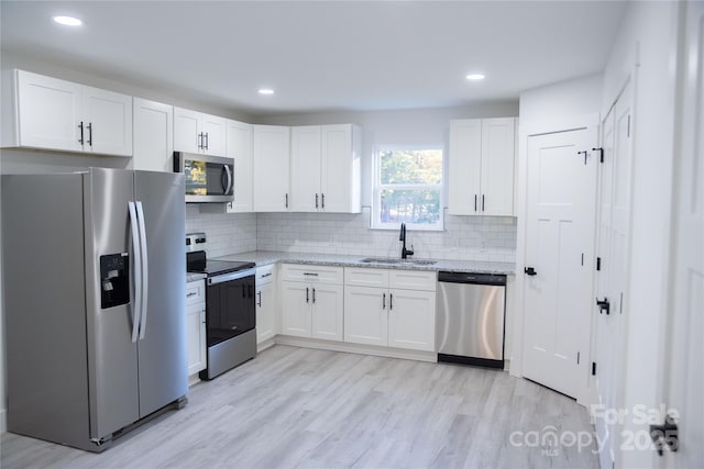 kitchen with white cabinets, appliances with stainless steel finishes, light stone counters, and sink