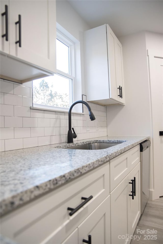 kitchen with light stone countertops, dishwasher, sink, decorative backsplash, and white cabinets