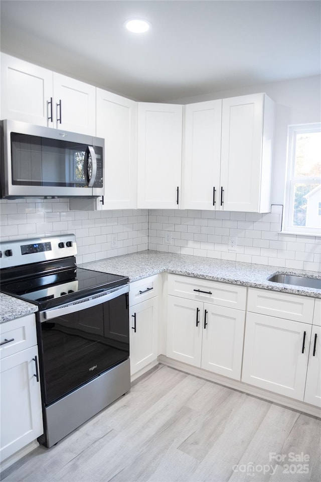 kitchen with sink, stainless steel appliances, white cabinetry, and light hardwood / wood-style flooring