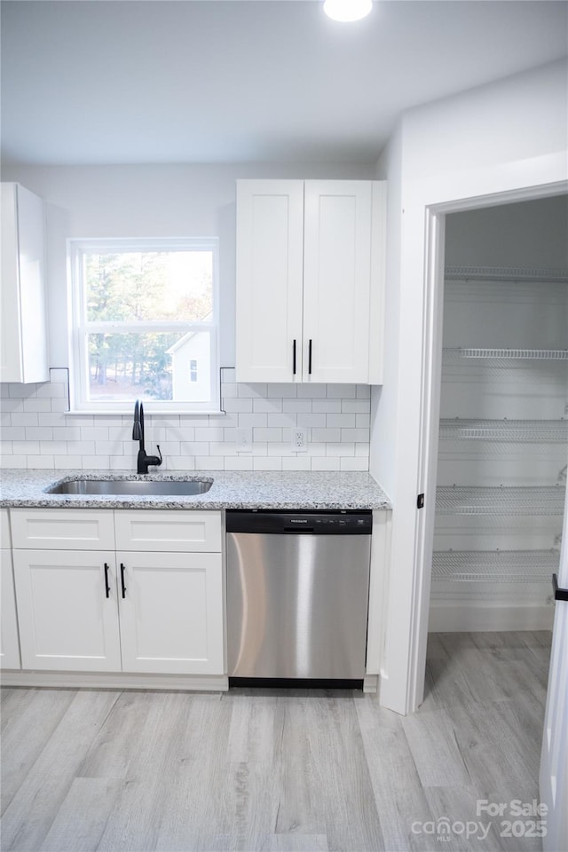 kitchen with stainless steel dishwasher, light stone counters, white cabinets, and sink